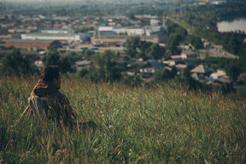 Obraz premium Man against the background of wild nature. Russian mountains, plains, fields. the traveler sits in the tall grass and looks into the distance