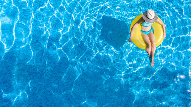Active young girl in swimming pool aerial top view from above, child relaxes and swims on inflatable ring donut and has fun in water on family vacation, tropical holiday resort
