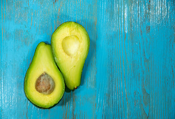 left on a blue wooden background - two halves of an avocado with bone inside