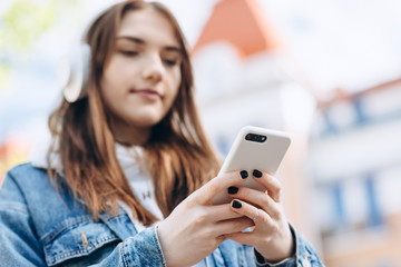 Fototapeta premium On a blurred background, a girl listens to music with wireless headphones from a smartphone on the street.