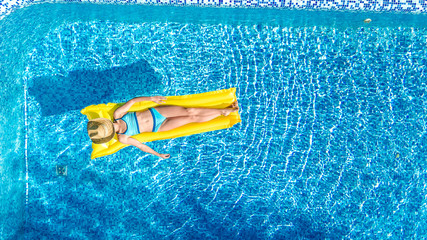 Girl relaxing in swimming pool, child swims on inflatable mattress and has fun in water on family vacation, tropical holiday resort, aerial drone view from above
