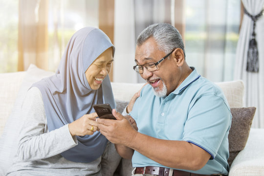 Senior couple laughing together while holding the smartphone