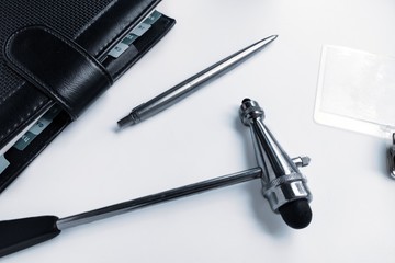 A stethoscope, a neurologist's hammer, a doctor's seal, a pen, and a black Notepad on a white background.