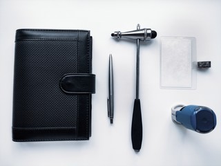 A stethoscope, a neurologist's hammer, a doctor's seal, a pen, and a black Notepad on a white background.