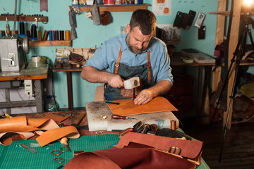 Leather craftsman working with natural leather using hammer. Handbag master at work in local workshop. Handmade concept.