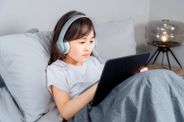 Asian little girl sitting on bed playing tablet