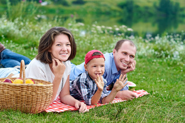 Fototapeta premium Happy family resting in nature. Mother, father and child Enjoying and lying on checkered plaid in meadow