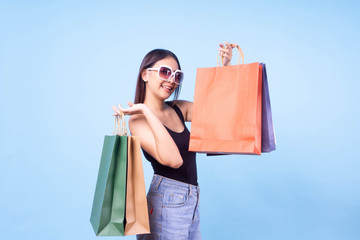 Asian woman wearing sunglasses shopping online in summer sale and carrying colorful shopping bag on isolated blue background,she smile and happy