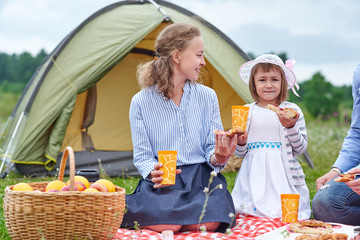 Happy family on picnic at camping. Mother and daughter eating near a tent in meadow or park