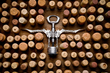 Wine corks of different sizes and a corkscrew standing upright on an old wooden surface. Background...