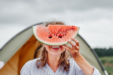 Funny woman eating watermelon on a picnic. Girl closed her eyes with a watermelon, looking into the holes