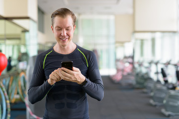 Portrait of happy young handsome man using phone at the gym during covid-19