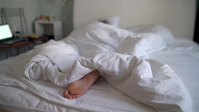 Woman sleeping in bed under white blanket, man touching womans bare feet.