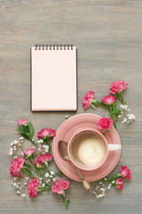 Obraz na płótnie Canvas Cup of creamy coffee, notepad and flowers