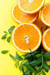 Creative summer background made half of oranges with leaves on yellow paper background.