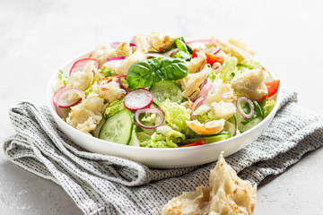 Delicious Fattoush or Arab salad with pita bread, fresh vegetables and basil on white plate. Middle Eastern bread salad.