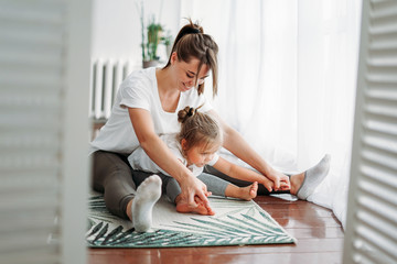 Happy mom and little daughter doing morning exercise together at the bright interior home