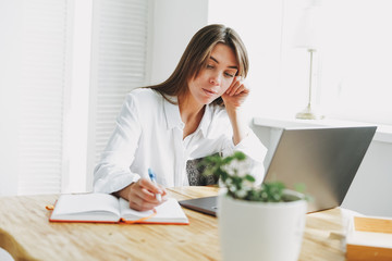 Working young brunette woman freelancer in casual clothes with laptop work at home in the bright interior