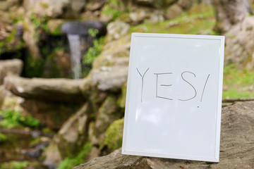 A sign that says "YES!" stands in front of a stream with a small waterfall.