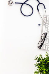 Doctor workplace. Stethoscope and computer keyboard on white office desk from above copy space