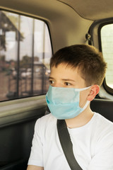 child boy sitting in a car  in a medical mask on his face as a measure of protection against viruses.