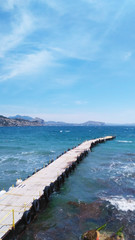 Photos from the phone. Seascape with a wooden pier for boats. Picturesque sea and mountains. Blue sky with clouds. Copy space.