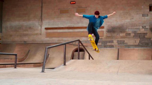 Young Caucasian skater wearing casual clothes and sneakers training skateboard flip on railing in modern skating arena