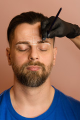 Permanent makeup for eyebrows. Tinting brows. Handsome man with eyebrows in barber shop. Brutal male with beard gets brow correction procedure. Master applying brow tint with brush. Brow care concept