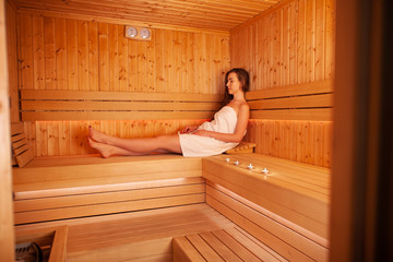 Fototapeta na wymiar Young beautiful woman have a rest in the sauna. Conception of bodycare. Young woman sitting on wooden bench in sauna.