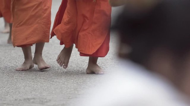 Slow motion shot of Buddhist monks wearing saffron robes while walking barefoot on street in city - Luang Prabang, Laos
