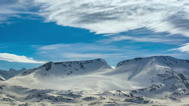 Waves of white feathery clouds passing on a blue sky above the snowcovered plateau in Jotunheimen National park in Norway.  Black jagger rocks peek from under the snow.