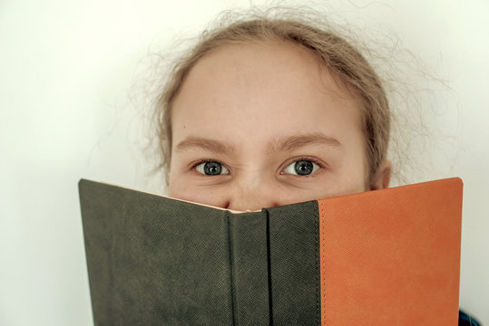 The Girl Closes Her Mouth With A Notepad. Close-up Of The Eye. Orange Book Cover.