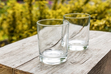Two empty glasses for water or cocktails on small wooden boards in the garden outside.