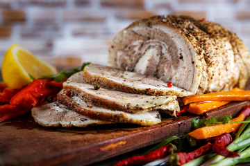Traditional sliced baked pork garnished with herbs, lemon carrots and spices, prepared for serving on the festive table, close-up, shallow depth of field, selective focus. The concept of delicious