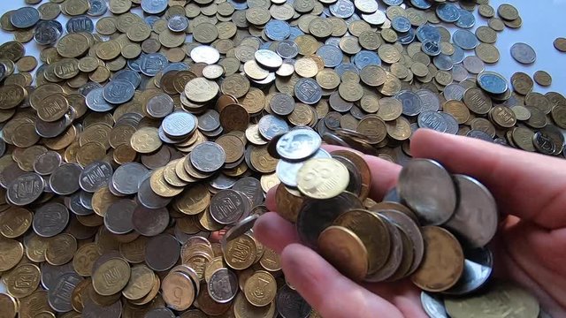 Person picks up handful of coins in hand and throws it over coins on table.