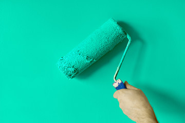 Left hand man's hand painting the wall with paint roller. Painting apartment, renovating with green color paint