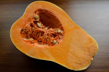 Primer plano de una calabaza anaranjada fresca y  aislada, cortada por la mitad, mostrando las semillas en su interior y sobre un fondo de madera.