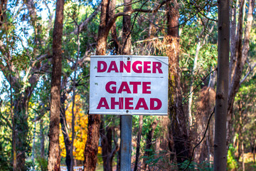 A striking red danger sign posted in the Australian bush in autumn, featuring yellow and green fall foliage.