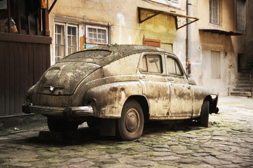 An old abandoned retro car with a leaking, rusty and rotten body with broken lights on a flat tire - one of the houses on Lviv street