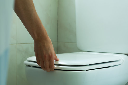 Mano levantando la tapa del inodoro.