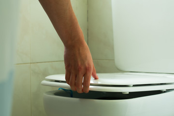 Fototapeta premium Mano levantando la tapa del baño en un cuarto blanco. 