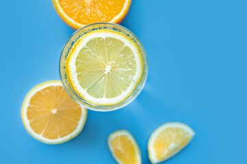 translucent glass of water with gases and bubbles, with a round slice of lemon on a glass and a whole lemon on blue background. Refreshment in the heat. Healthy lifestyle and nutrition, top view