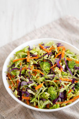 Homemade Raw Shredded Broccoli Slaw in a white bowl on a white wooden background, side view. Space for text.