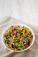 Homemade Raw Shredded Broccoli Slaw in a white bowl on a white wooden surface, side view. Copy space.