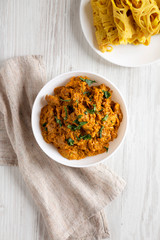Homemade Chicken Tikka Masala in a white bowl on a white wooden table, top view. Flat lay, overhead, from above.