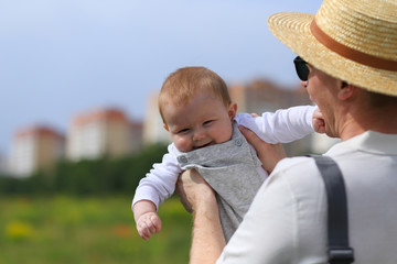 dad with a baby of eight months have fun playing in the grass in the sun in the park on the background of houses