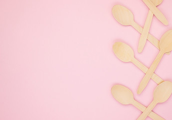 Eco-friendly biodegradable compostable wooden spoons on a soft pink background. Wooden spoons are gathered together on the right side. Background for the holidays