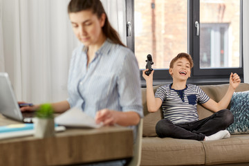 leisure, technology and children concept - happy smiling boy with gamepad playing video game and celebrating success at home