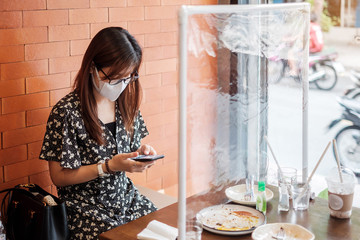 Asian woman using smartphone during dining time in restaurant with separated of shield plastic...
