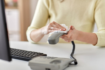 hygiene and disinfection concept - close up of woman hands cleaning desk phone with paper tissue